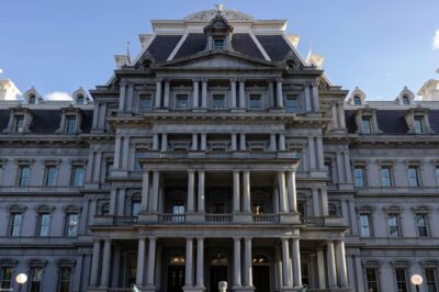 Front view of the Eisenhower Executive Office Building, which houses the U.S. Office of Management and Budget, showing the historic government building's rows of windows, ornate columns, and central staircase under a clear blue sky.