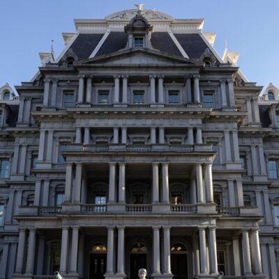 Front view of the Eisenhower Executive Office Building, which houses the U.S. Office of Management and Budget, showing the historic government building's rows of windows, ornate columns, and central staircase under a clear blue sky.