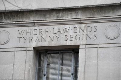 Engraved words on the facade of the U.S. Department of Justice building read "WHERE LAW ENDS TYRANNY BEGINS," above a window set into the stone exterior.