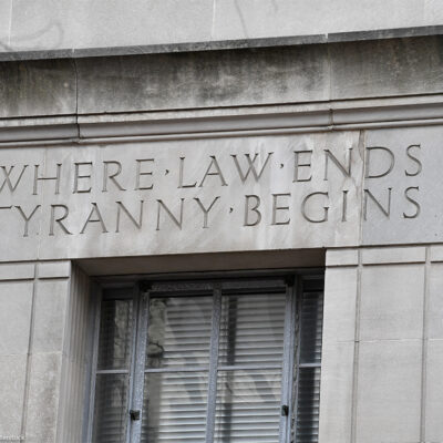 Engraved words on the facade of the U.S. Department of Justice building read "WHERE LAW ENDS TYRANNY BEGINS," above a window set into the stone exterior.