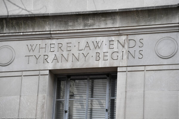 Engraved words on the facade of the U.S. Department of Justice building read "WHERE LAW ENDS TYRANNY BEGINS," above a window set into the stone exterior.