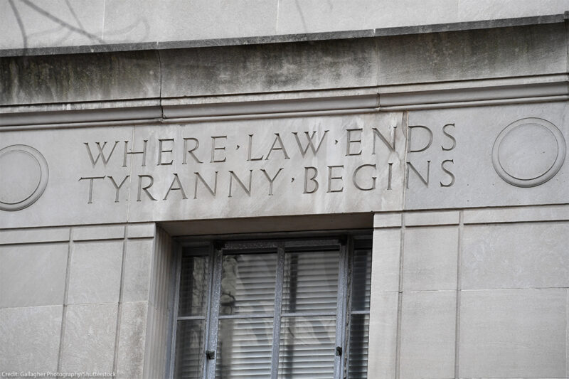 Engraved words on the facade of the U.S. Department of Justice building read "WHERE LAW ENDS TYRANNY BEGINS," above a window set into the stone exterior.