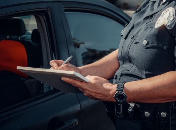 A police officer writing a report next to a car.