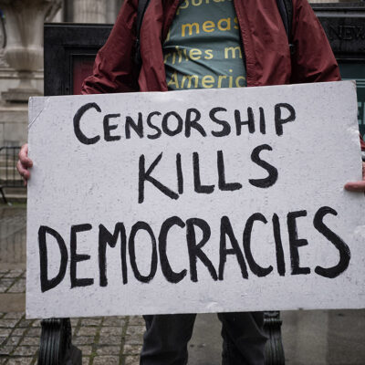A demonstrator holding a sign that says "Censorship Kills Democracies."
