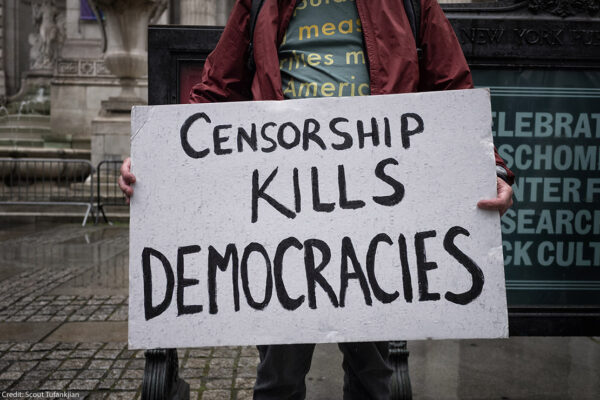 A demonstrator holding a sign that says "Censorship Kills Democracies."
