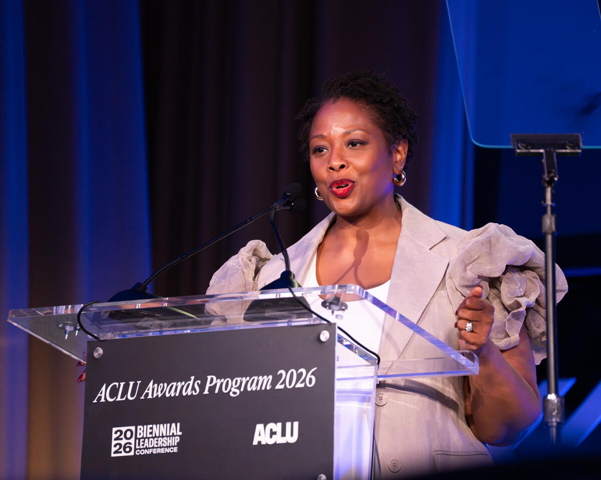 ACLU President Deborah Archer, a Black woman in formal dress and a tan coat, speaks from the stage at a clear podium with a plaque that reads ACLU Award Program 2026.