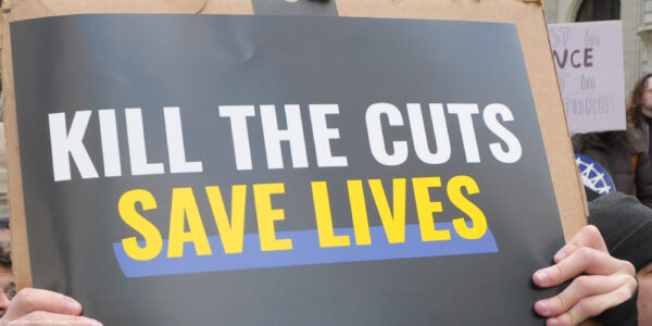 A demonstrator holds up a sign during a protest that reads "KILL THE CUTS, SAVE LIVES".