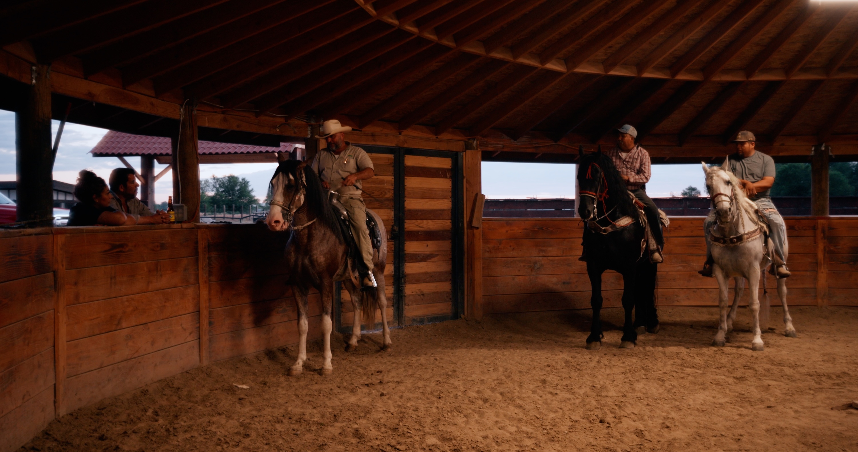 Three individuals riding horses in a stable.