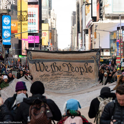 People carrying a large banner with the Preamble to the U.S. Constitution through Times Square.