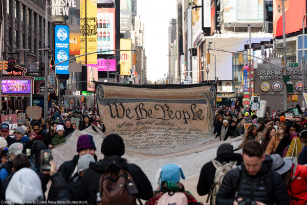 People carrying a large banner with the Preamble to the U.S. Constitution through Times Square.