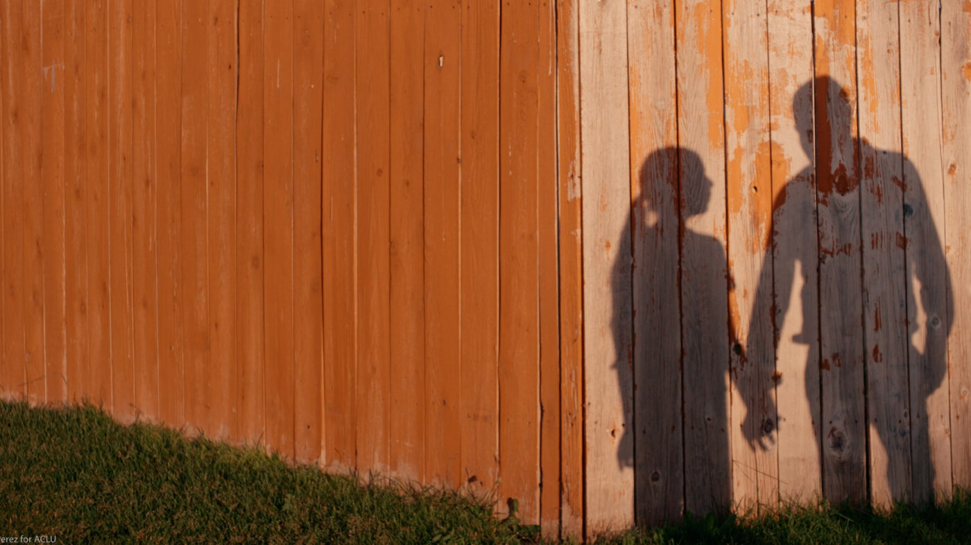 Shadows against a wooden wall of two individuals holding hands.