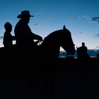 The silhouette of a man and a child on a horse.