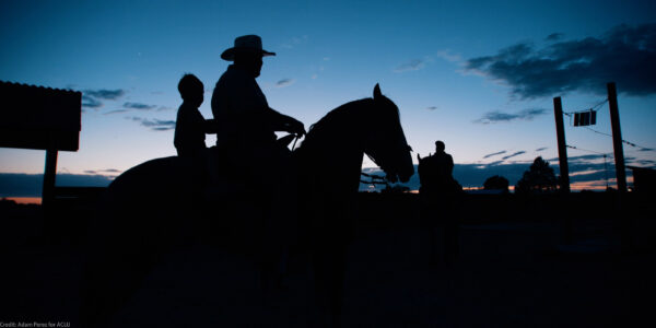 The silhouette of a man and a child on a horse.